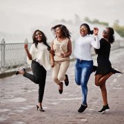 Group of four african american girls having fun and jumping against lake with fountains.